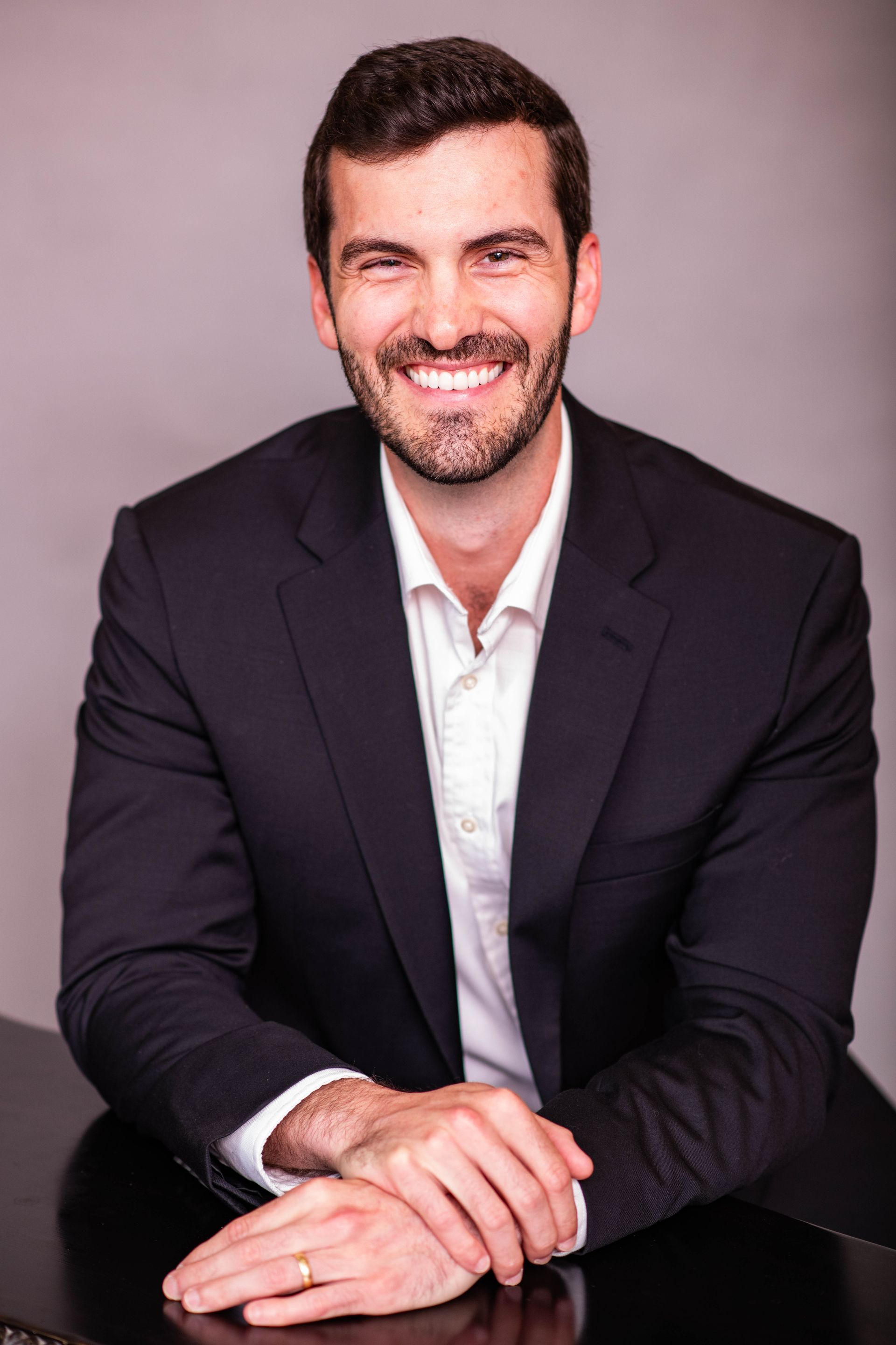 A man in a suit and white shirt is sitting at a table with his hands folded.