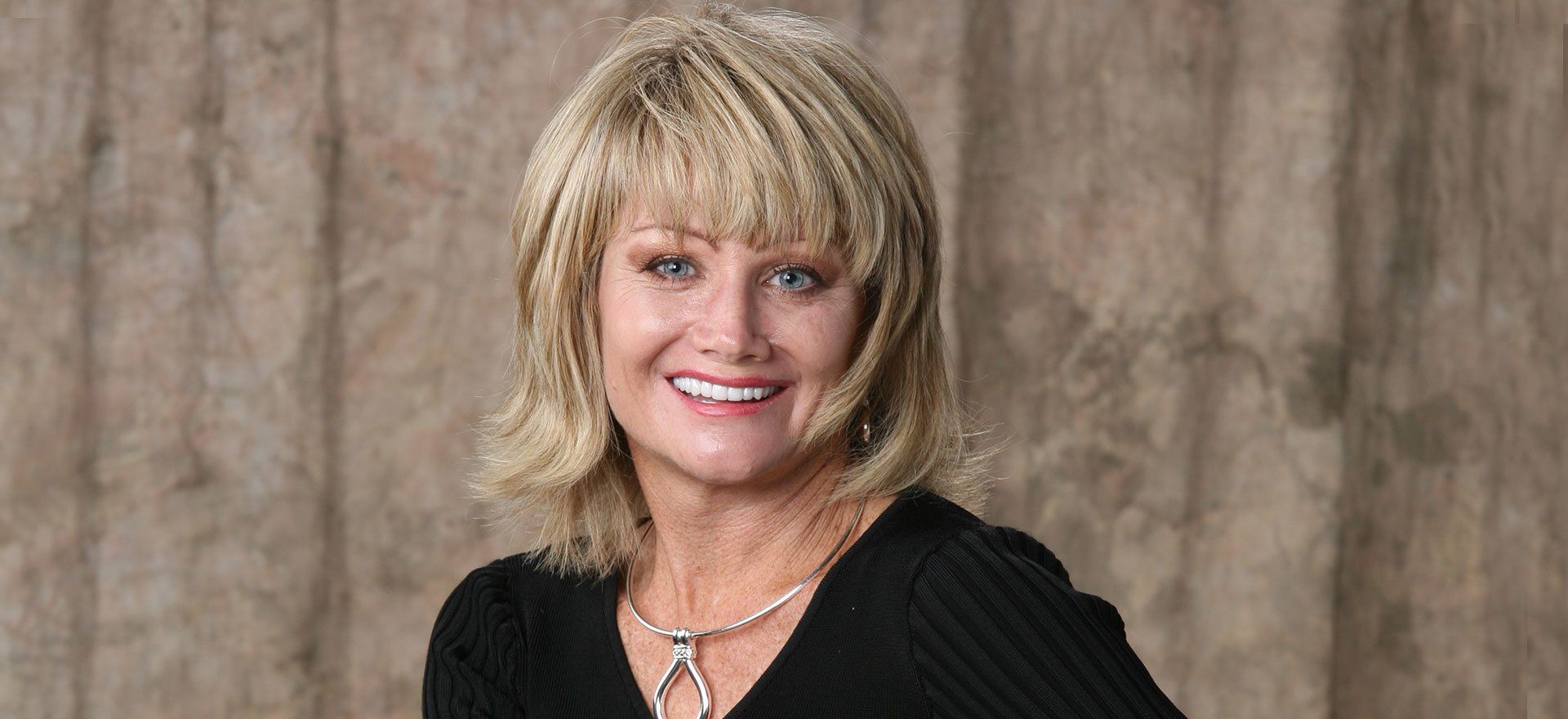 A woman wearing a black shirt and a necklace is smiling for the camera.