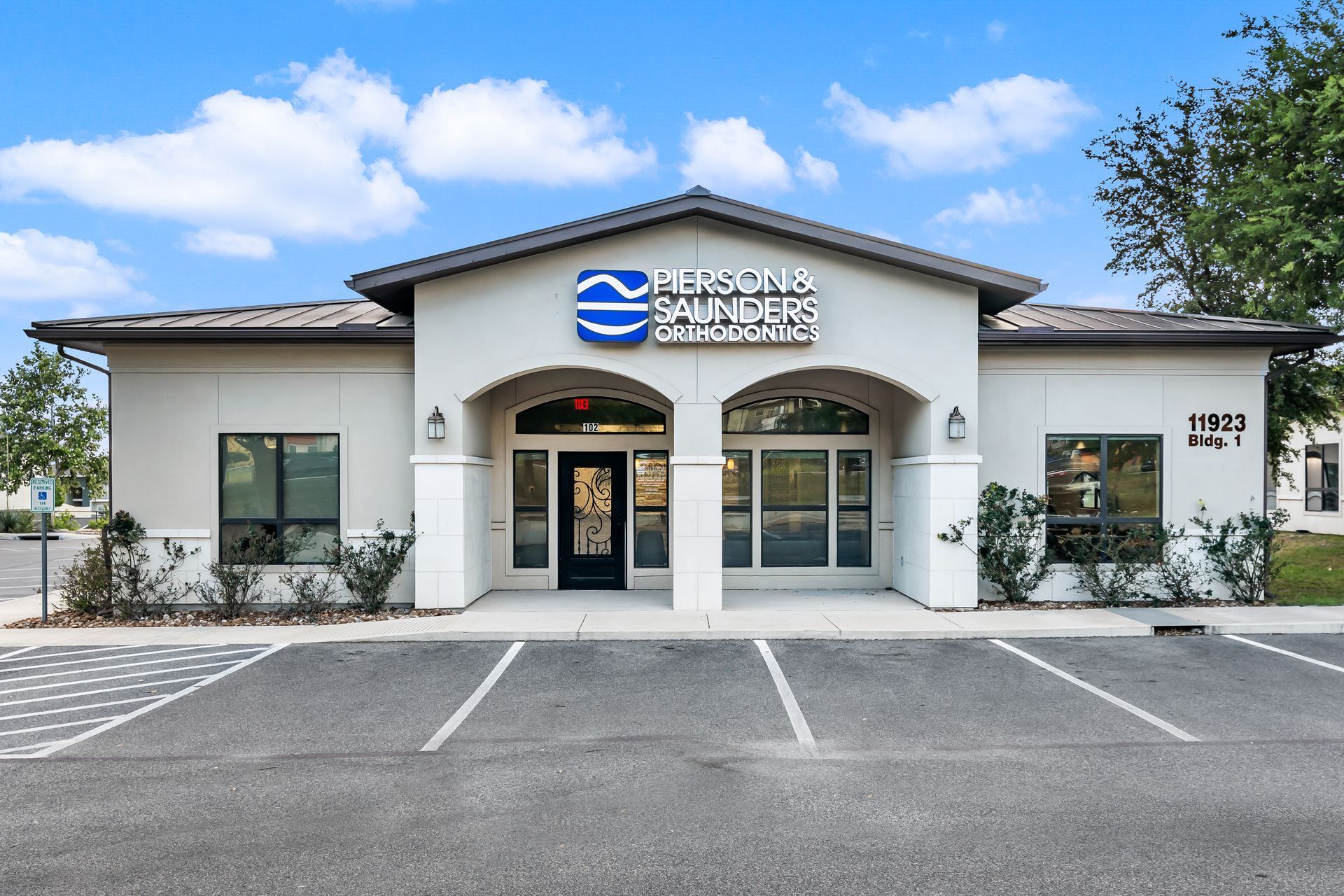 A one-story commercial building with a beige facade, a dark roof, and a central entrance under an arched portico.