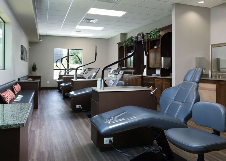 A modern aesthetic treatment room featuring rows of dark grey reclining chairs, workstations, and soft interior lighting.
