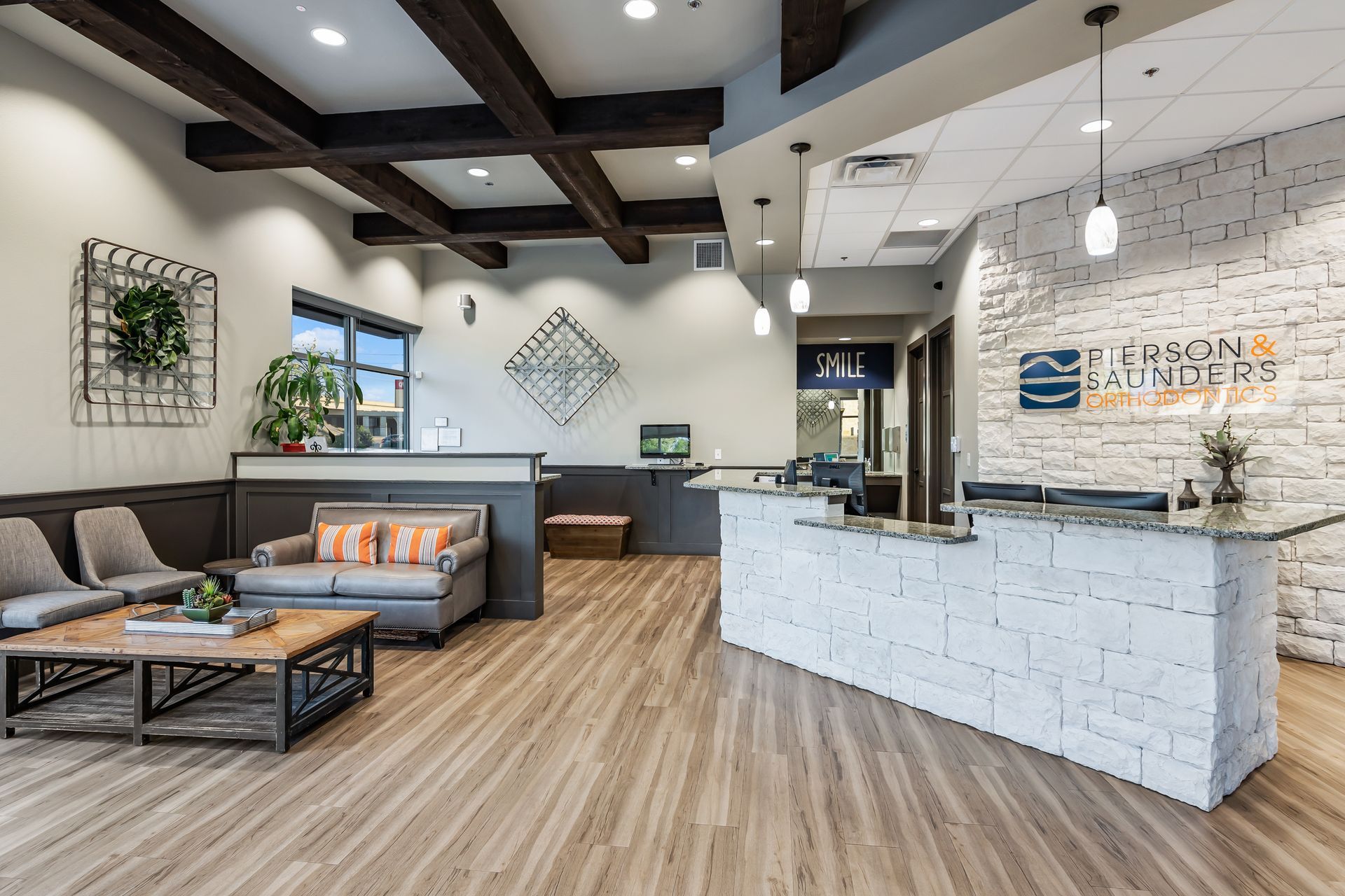 Modern lobby with a white stone reception desk, wooden ceiling beams, grey sofa, chairs, and wood-patterned flooring.