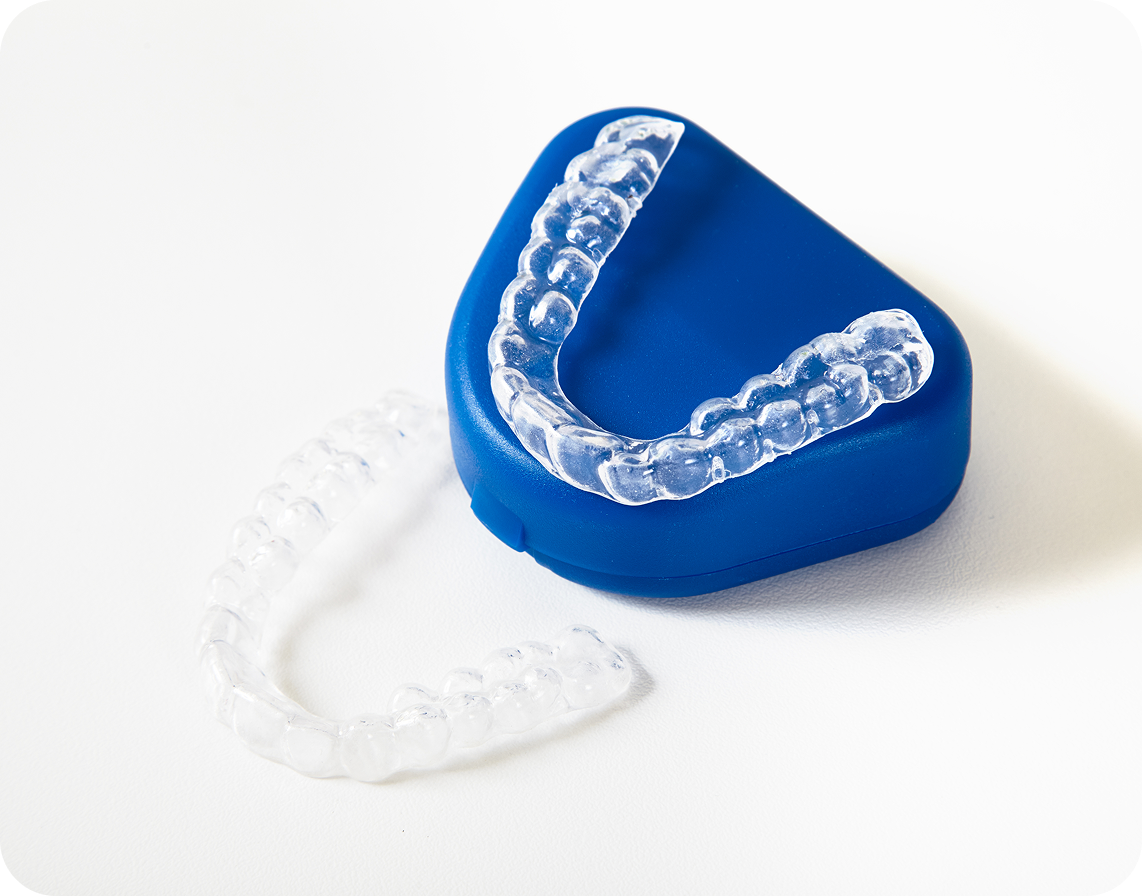 Clear plastic orthodontic retainers, one resting on a blue case and one placed on a white surface.