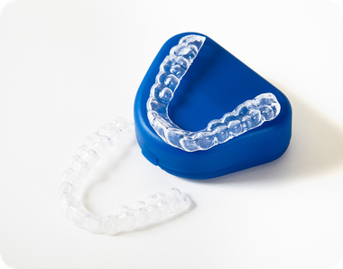 Clear plastic orthodontic retainers, one resting on a blue case and one placed on a white surface.