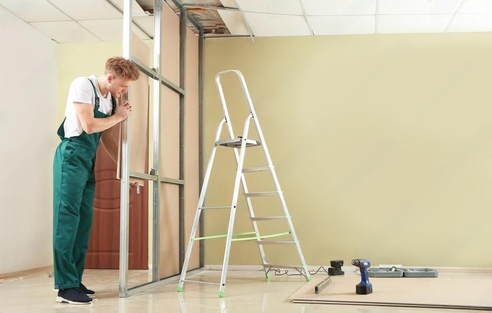 a man is standing next to a ladder and working on a wall .