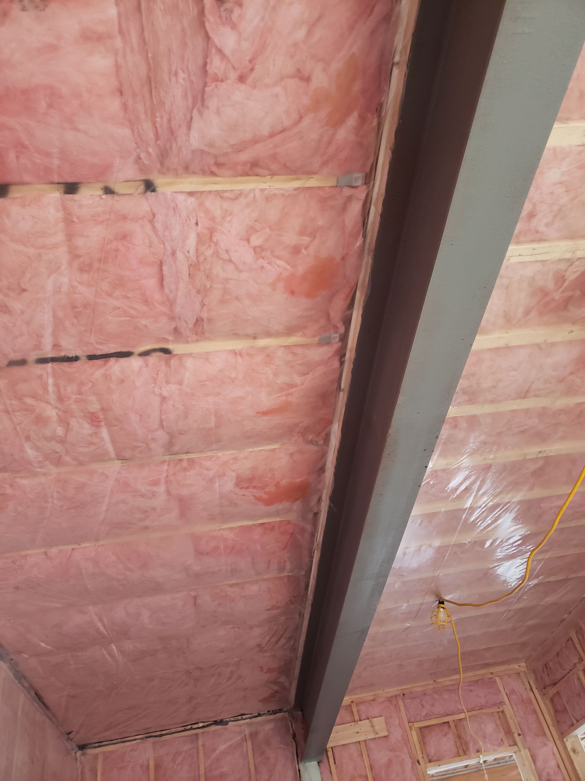 Un plafond avec une isolation rose et une poutre métallique.