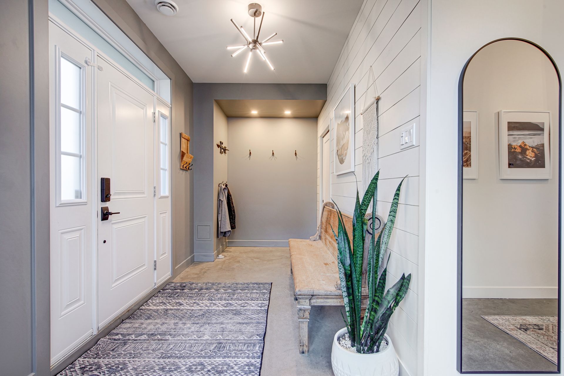 Un couloir avec des portes blanches, un banc, une plante et un miroir.