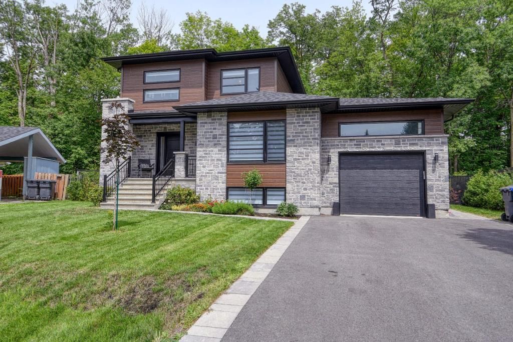 Une grande maison avec un garage et une allée est entourée d'arbres.