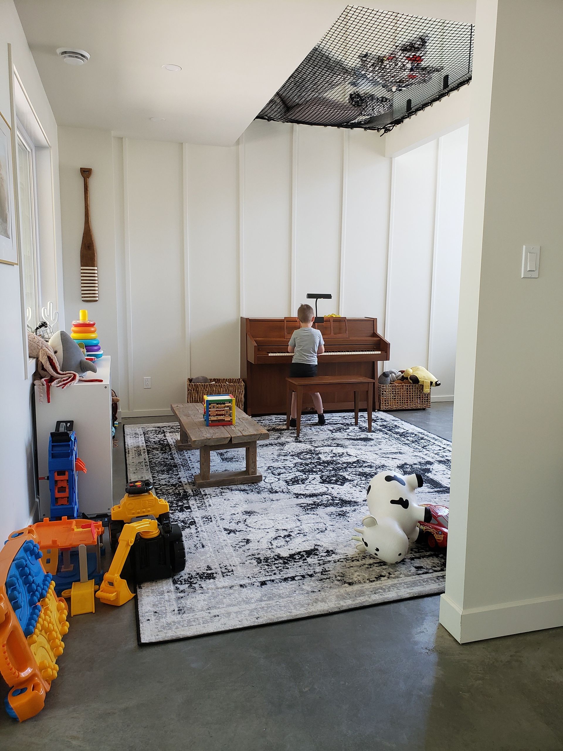 Un petit garçon joue du piano dans une pièce remplie de jouets.