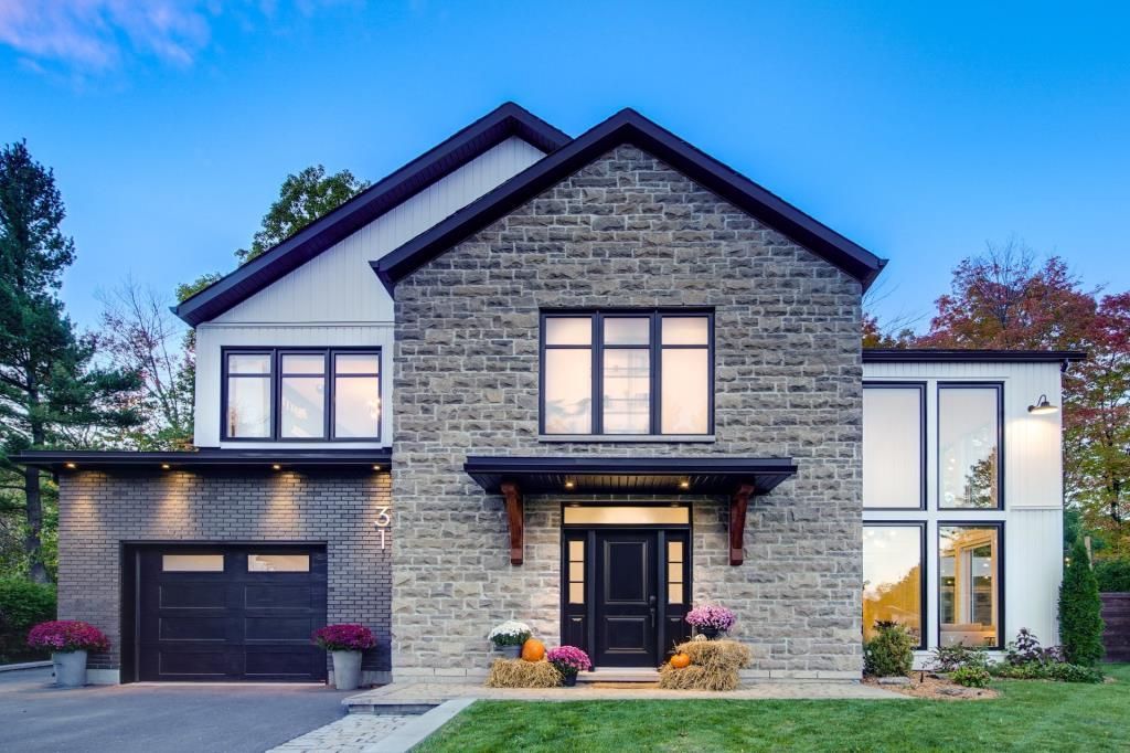 Une grande maison en briques avec une porte de garage noire est assise sur une pelouse verte luxuriante.