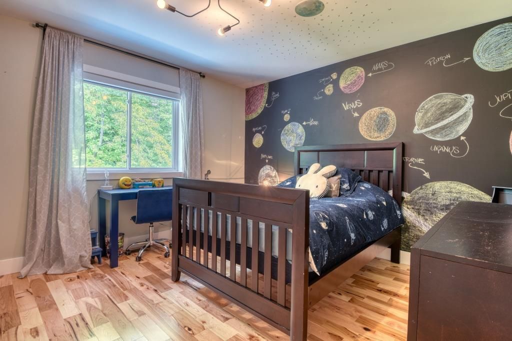 Une chambre avec un lit, un bureau et un mur en tableau noir avec des planètes dessus.