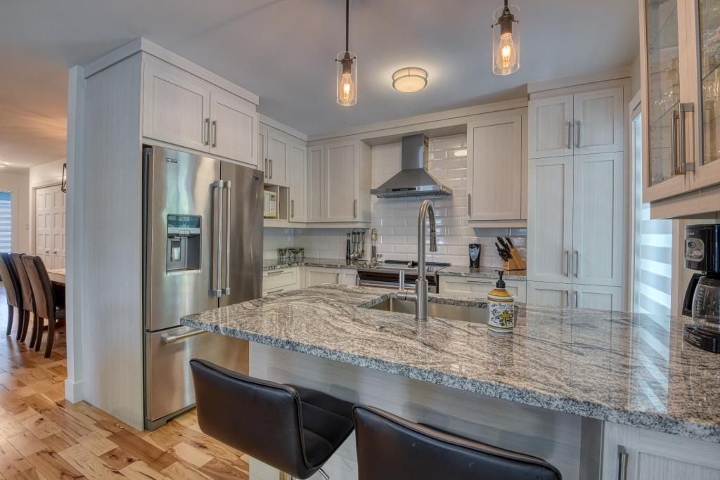 Une cuisine avec comptoirs en granit, appareils électroménagers en acier inoxydable et armoires blanches.