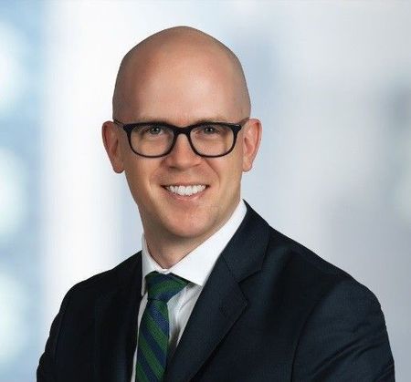 A bald man wearing glasses and a suit is smiling for the camera.