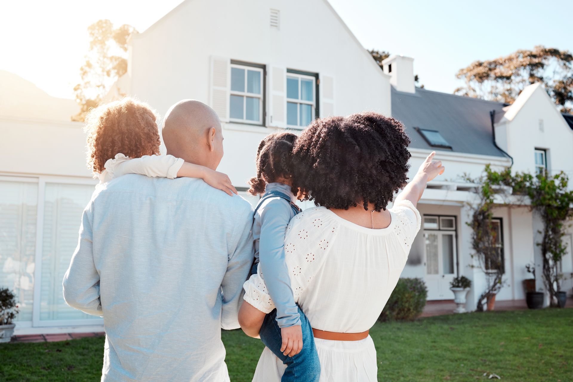 A family is standing in front of a white house looking at it.