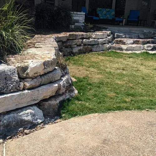 Stone retaining wall and steps next to a grassy lawn and concrete patio.