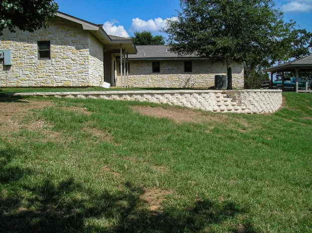 Stone house with a retaining wall and green lawn.