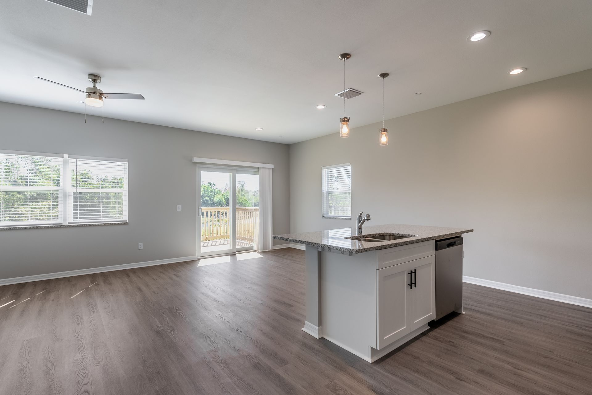 an empty living room with a kitchen and a ceiling fan and an island