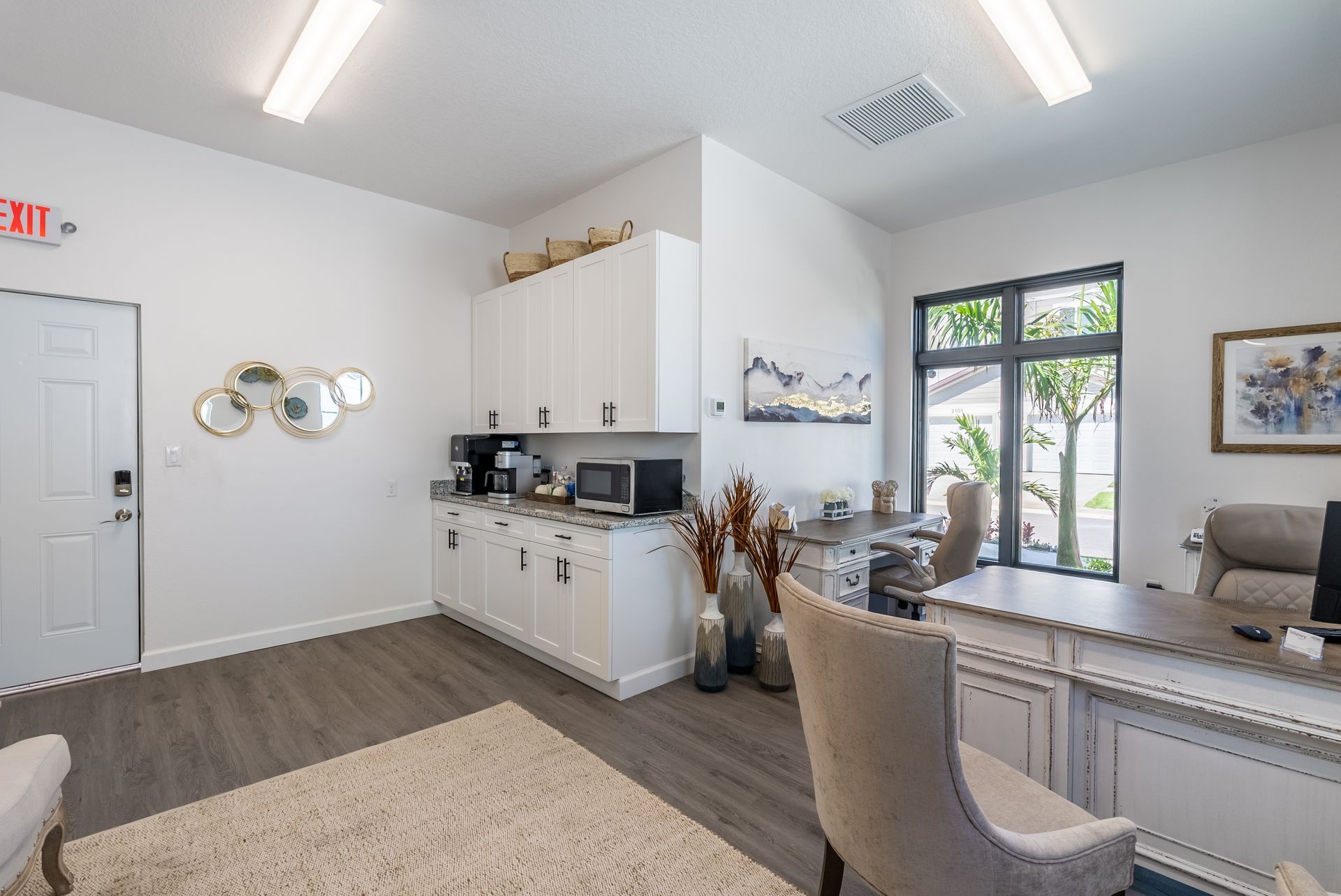 a living room with a desk , chairs , and a large window .