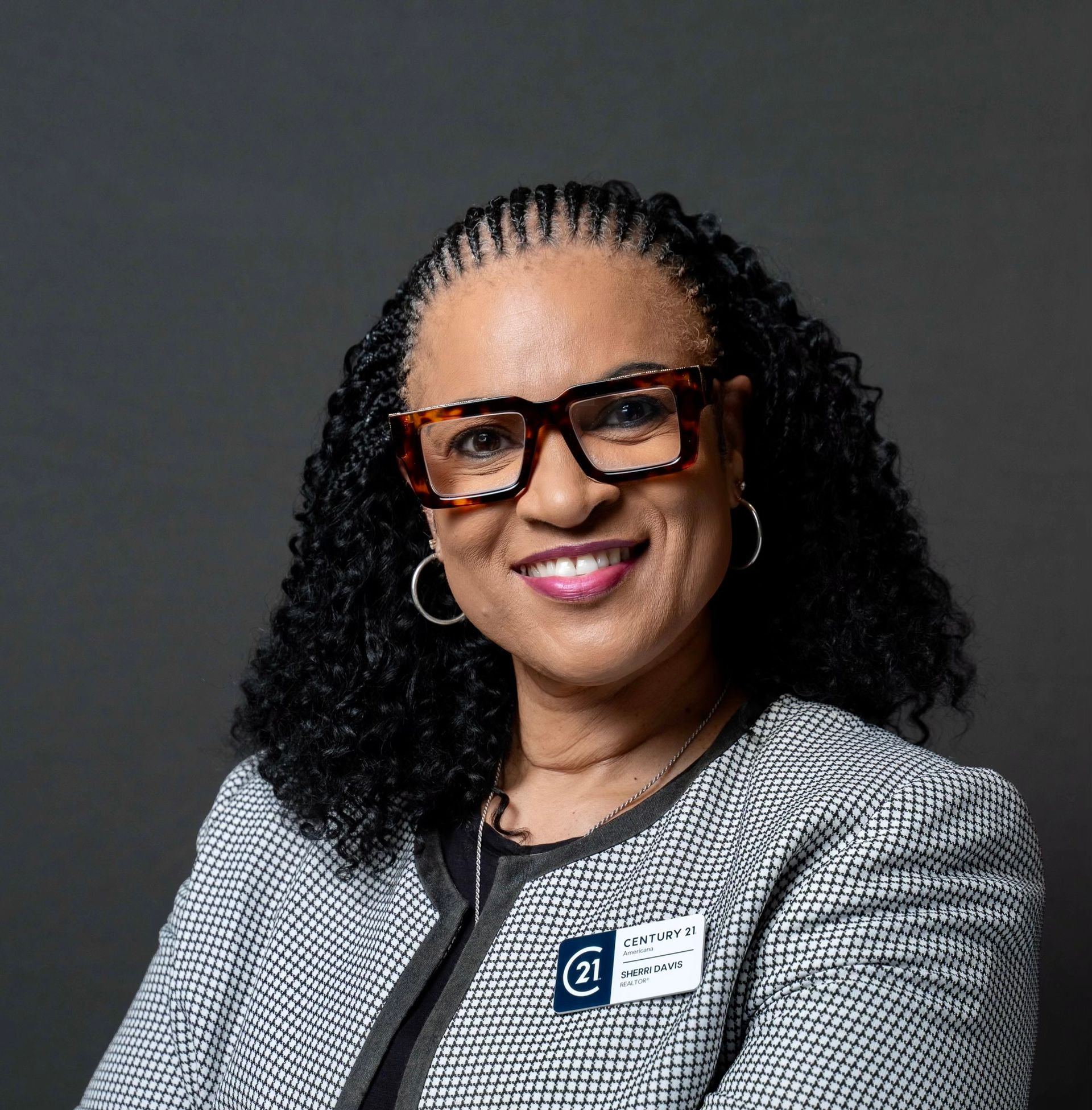 Woman wearing glasses, smiling, wearing a blazer with a name tag.