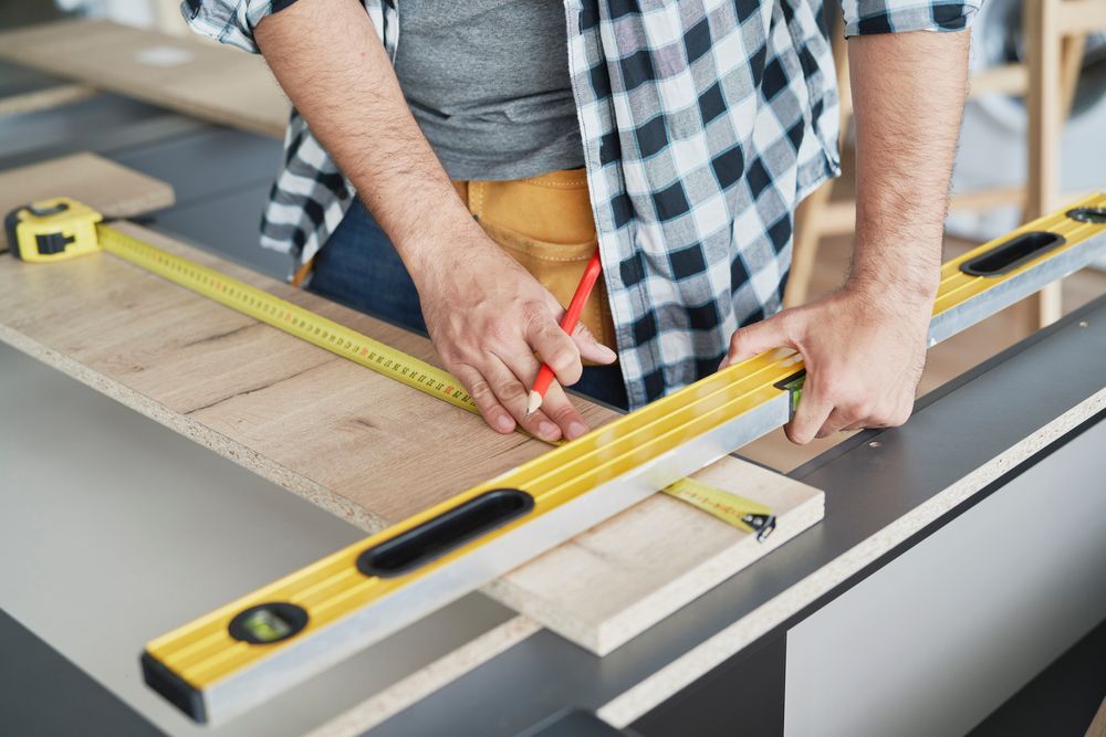 A man is measuring a piece of wood with a tape measure and a pencil.