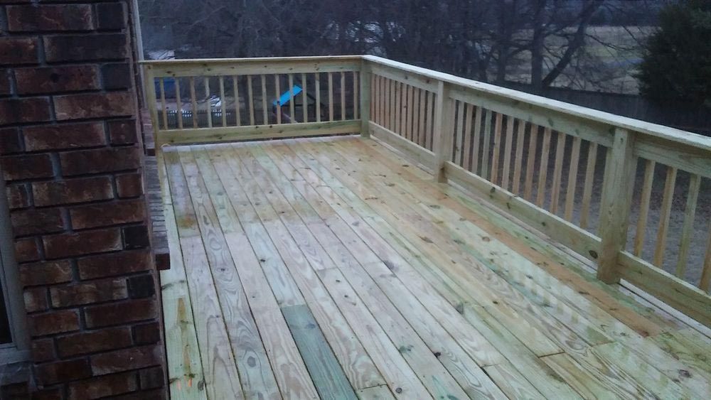 A large wooden deck with a railing and a brick wall.