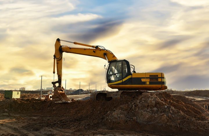 A yellow excavator is sitting on top of a pile of dirt at a construction site.