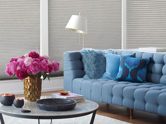 Living room with a blue couch, vase of flowers, and windows with grey shades