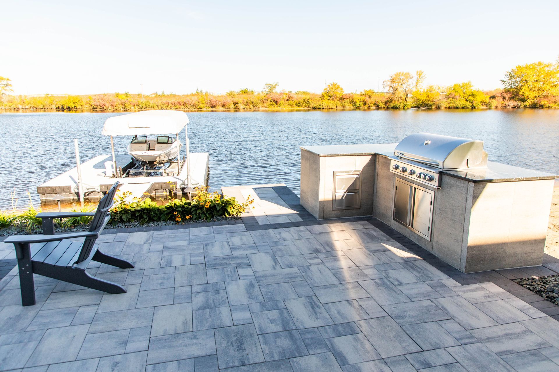 A patio with a grill and chairs next to a lake.