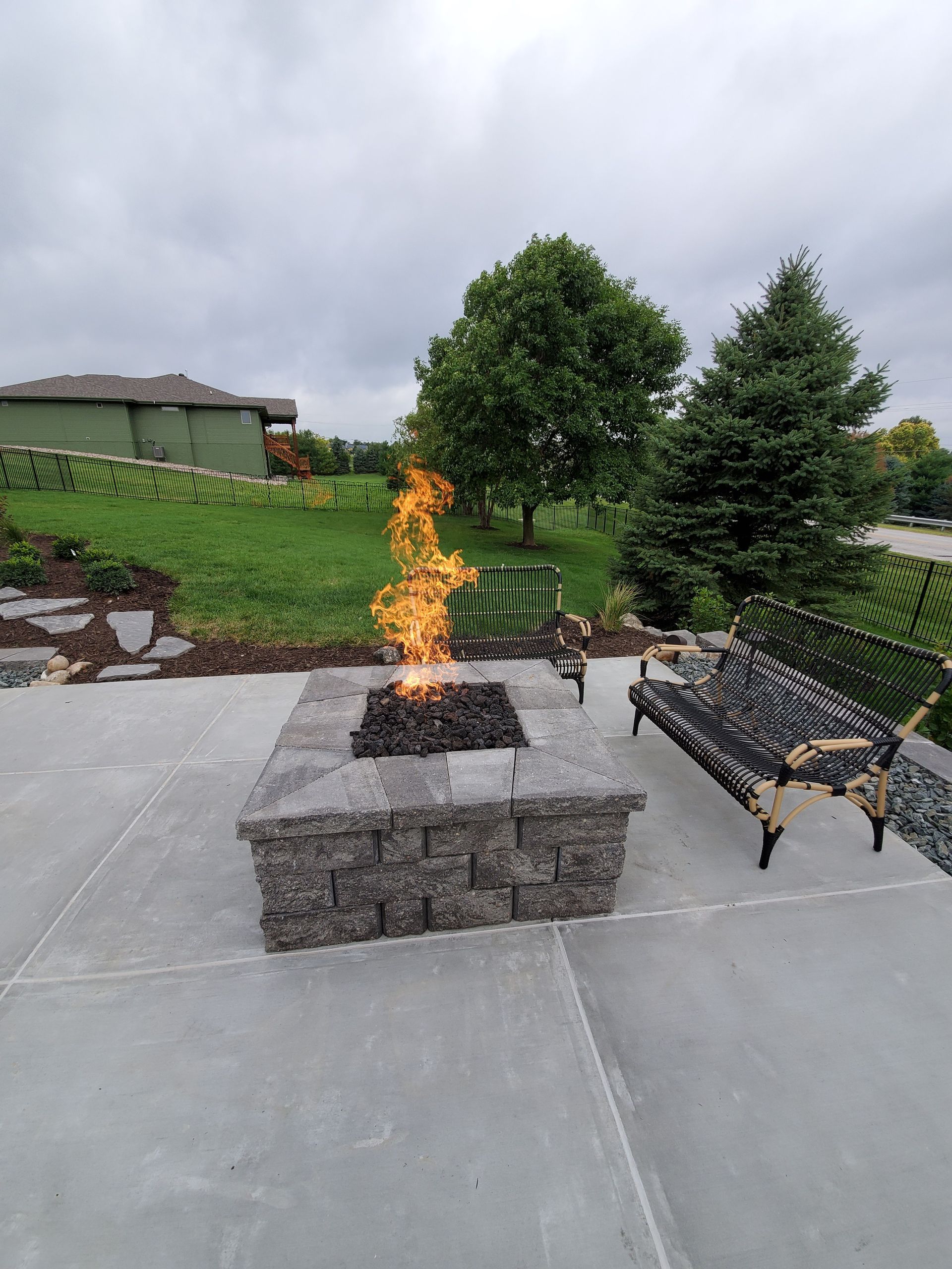 A fire pit is sitting on top of a concrete patio next to a bench.