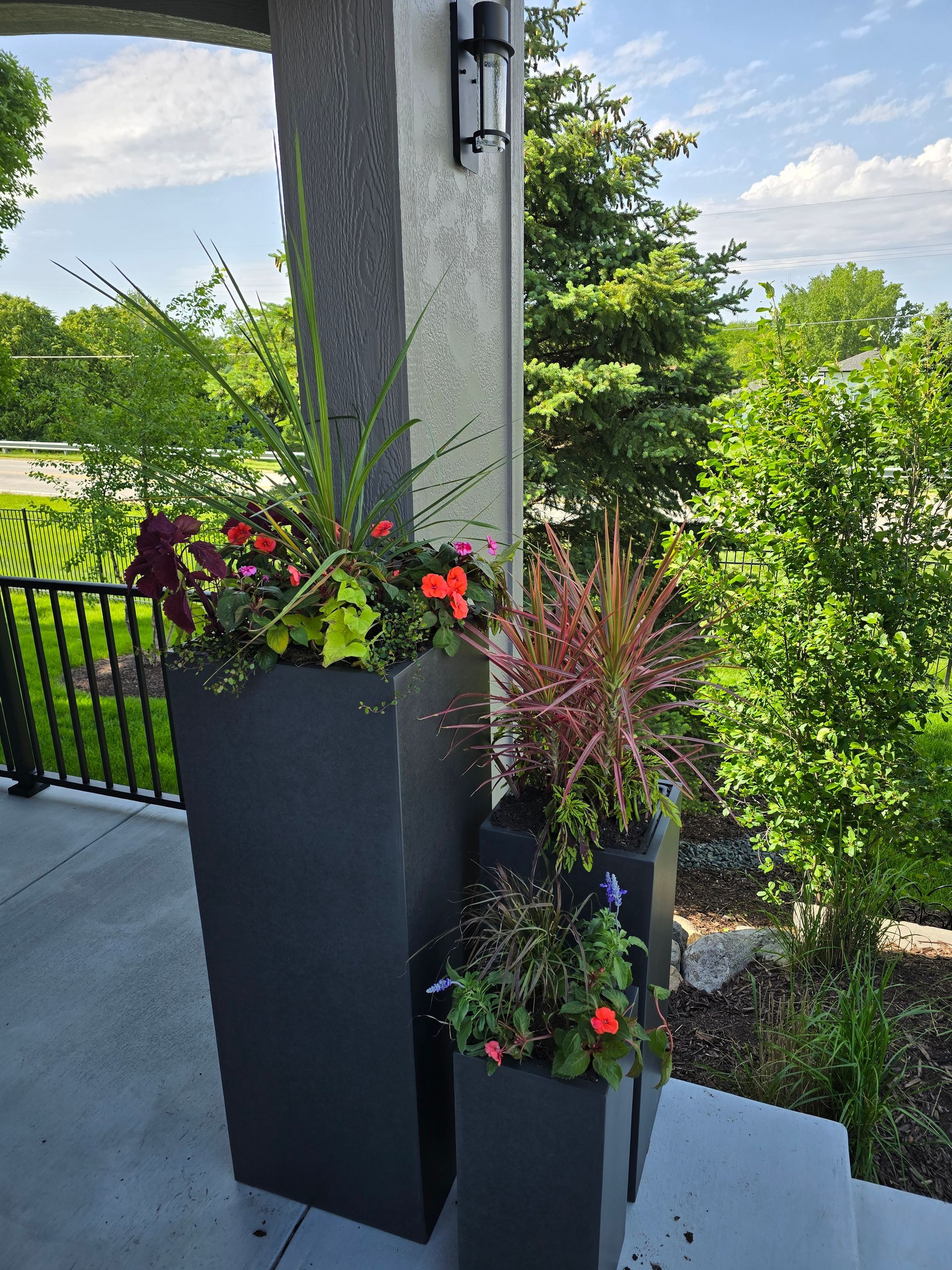 Three gray planters with colorful flowers on a porch.