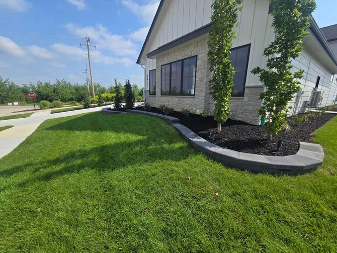 A modern white house with a stone facade, featuring a curved stone retaining wall surrounding a landscaped garden bed.