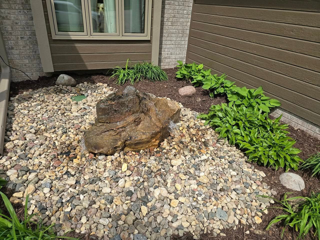 There is a large rock in the middle of a rock garden in front of a house.