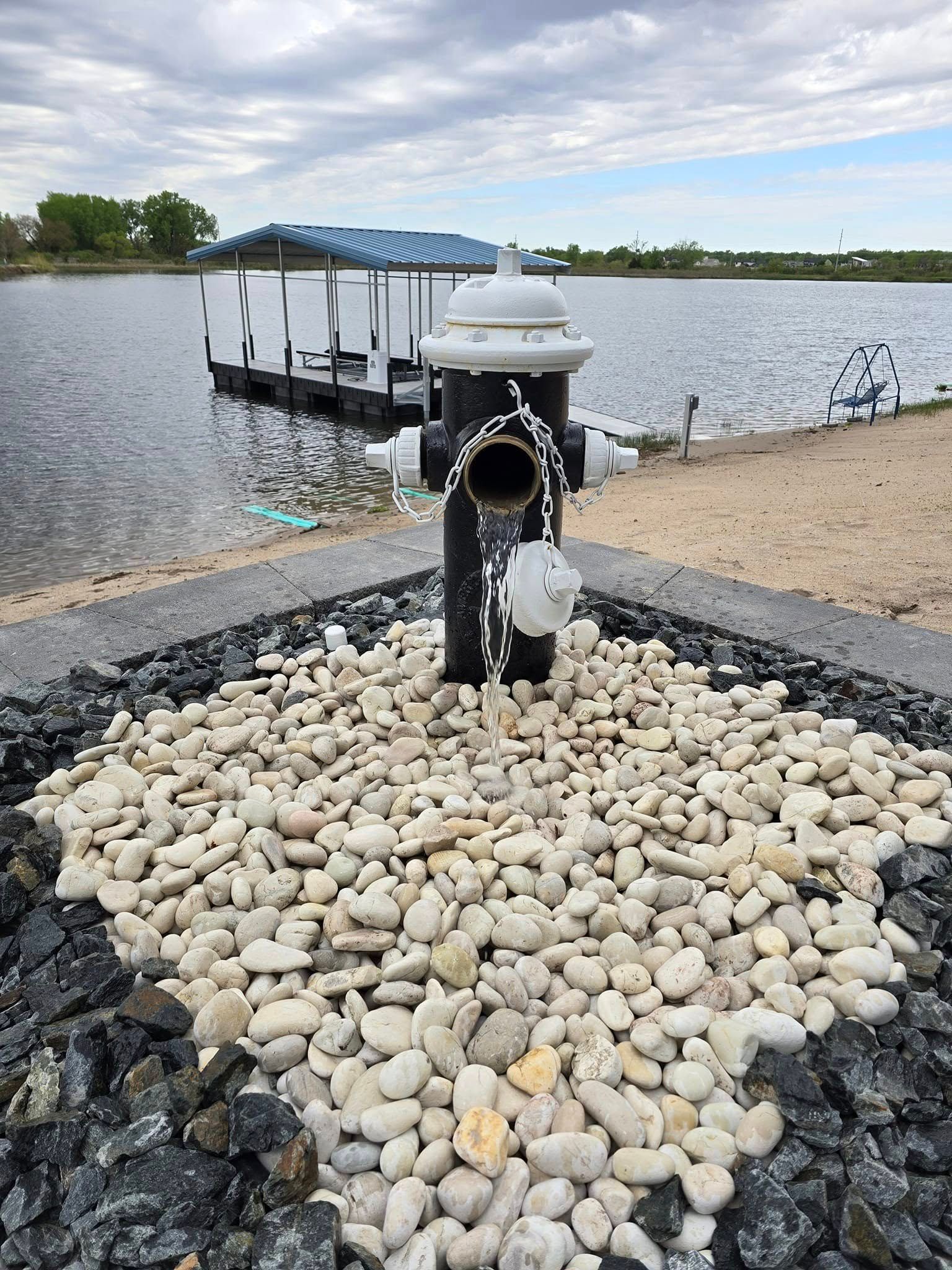 A fire hydrant is sitting on top of a pile of rocks next to a lake.