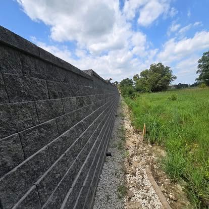 A brick wall surrounds a grassy field on a sunny day.