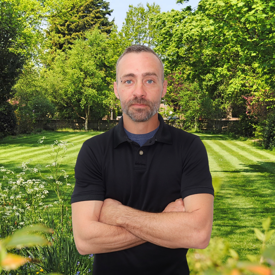 A man with his arms crossed in front of a lush green field