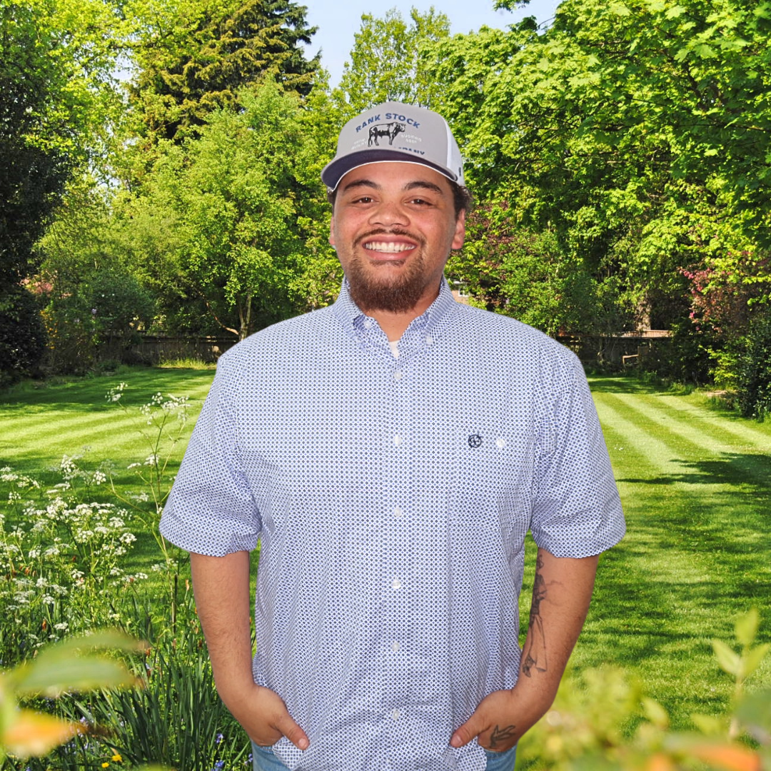 A man wearing a hat is standing in front of a lush green field.