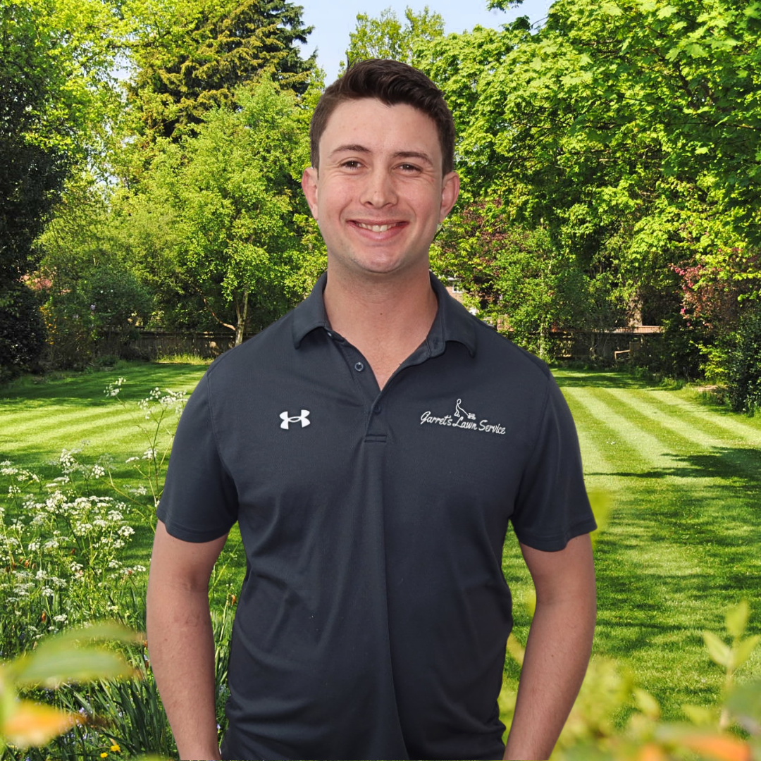 A man wearing a black under armour shirt is standing in front of a lush green field.