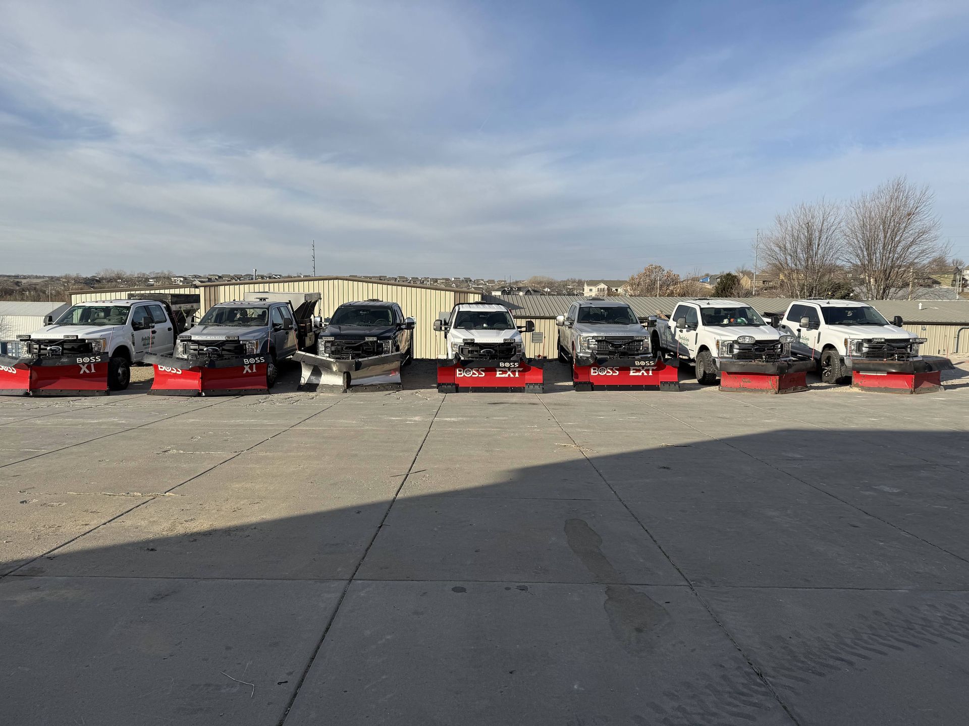 Several snowplow trucks parked on pavement under a cloudy sky.