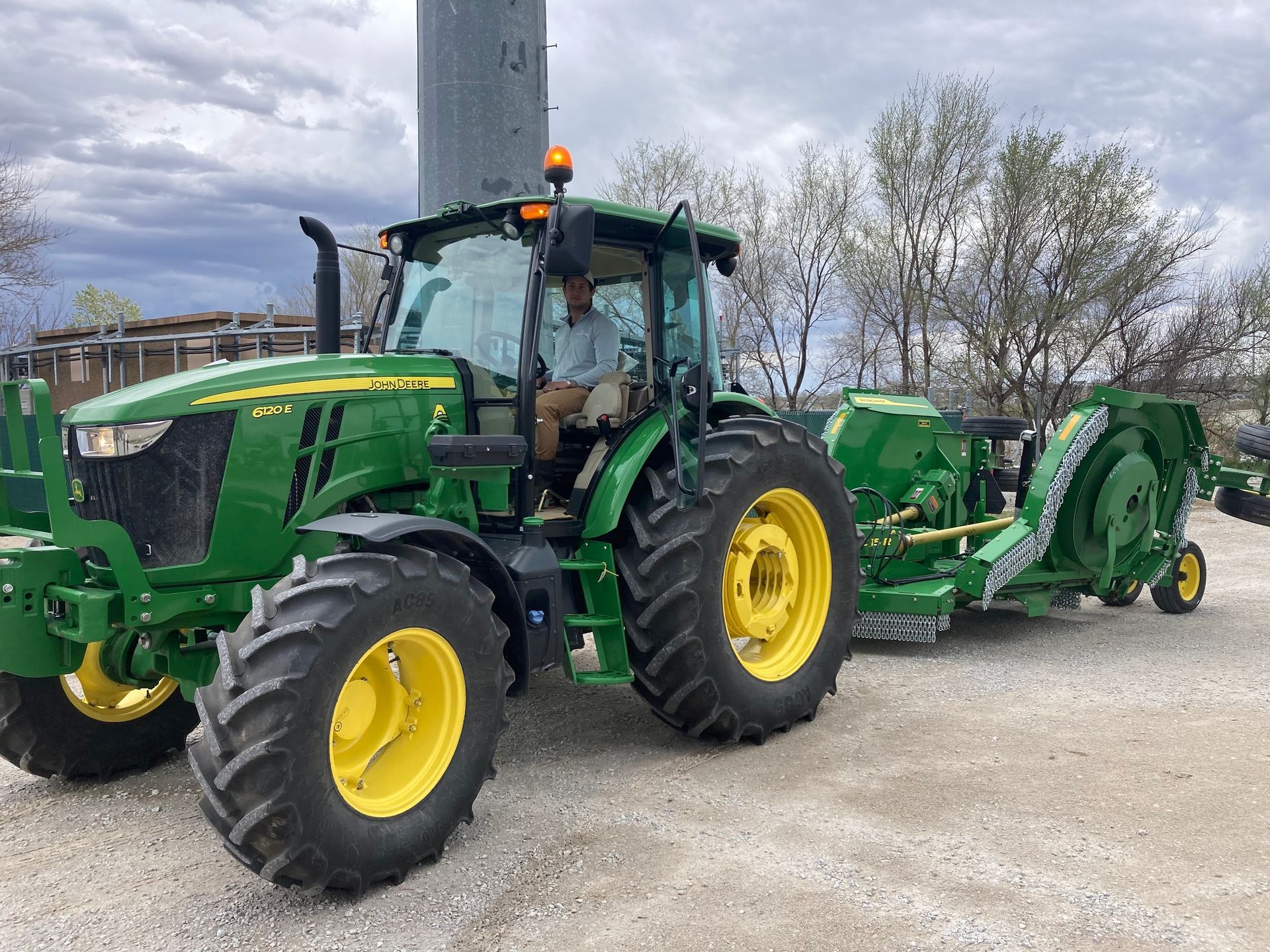 A man is driving a green john deere tractor with a trailer attached to it.