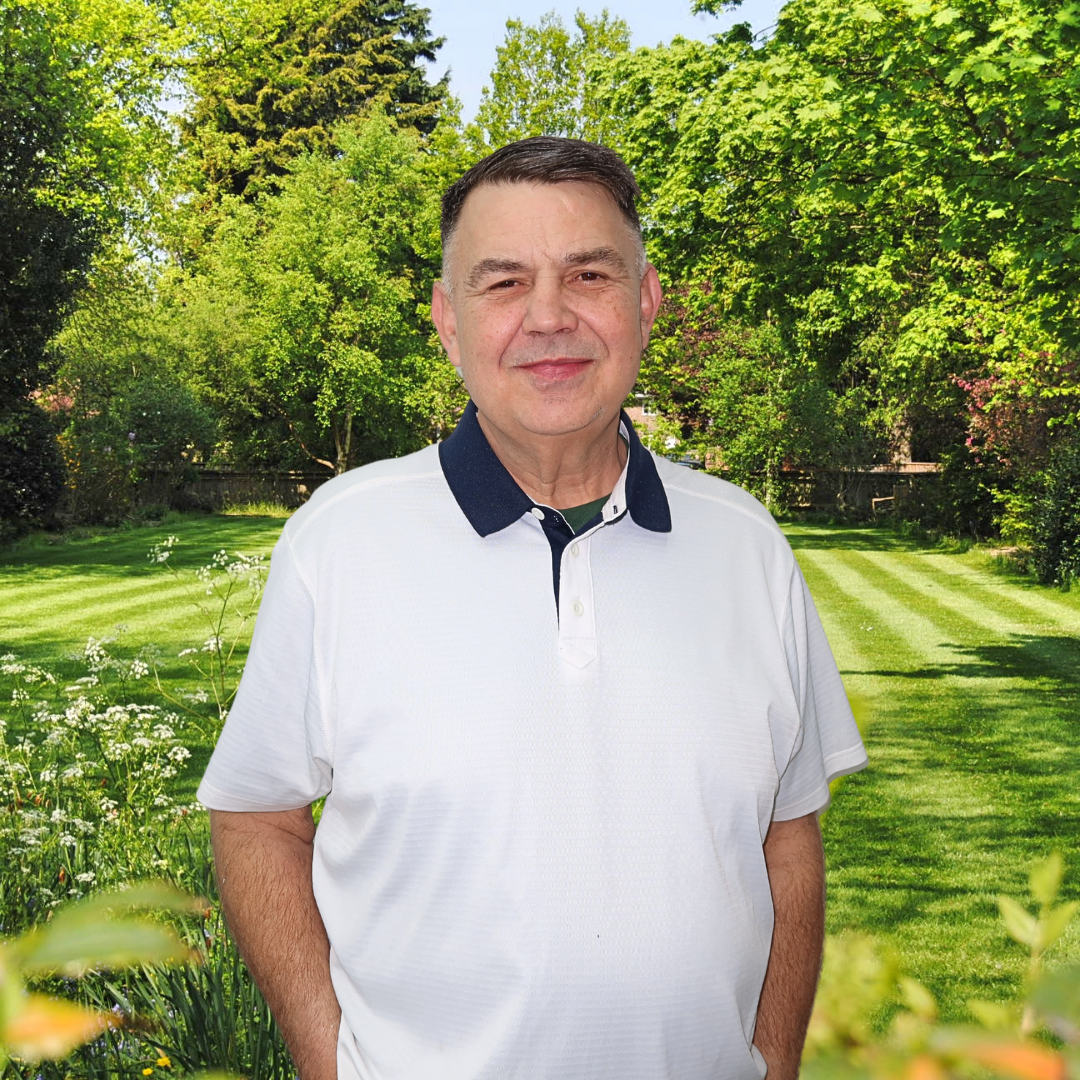 A man in a white shirt is standing in front of a lush green field.