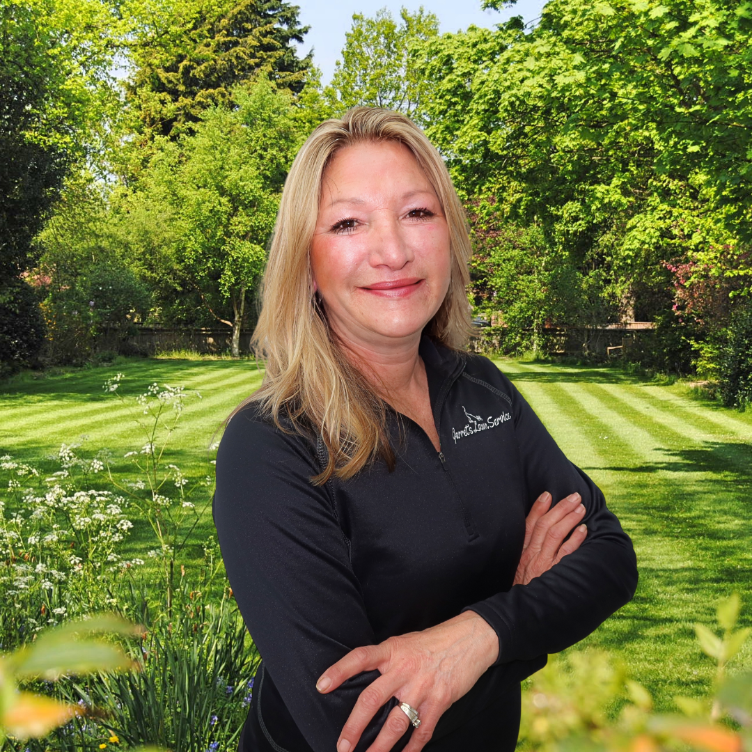 A woman in a black shirt is standing in a garden with her arms crossed