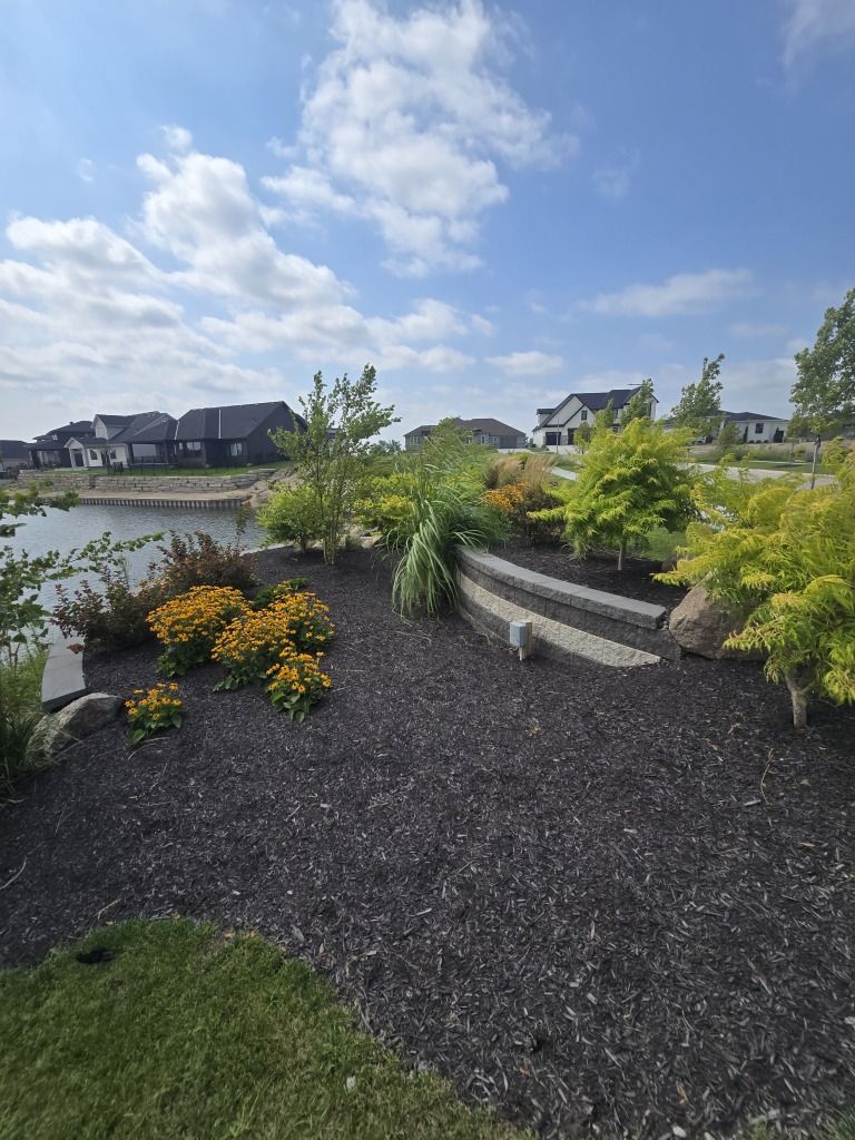 Landscaped garden with pond, plants, and homes under a blue sky.