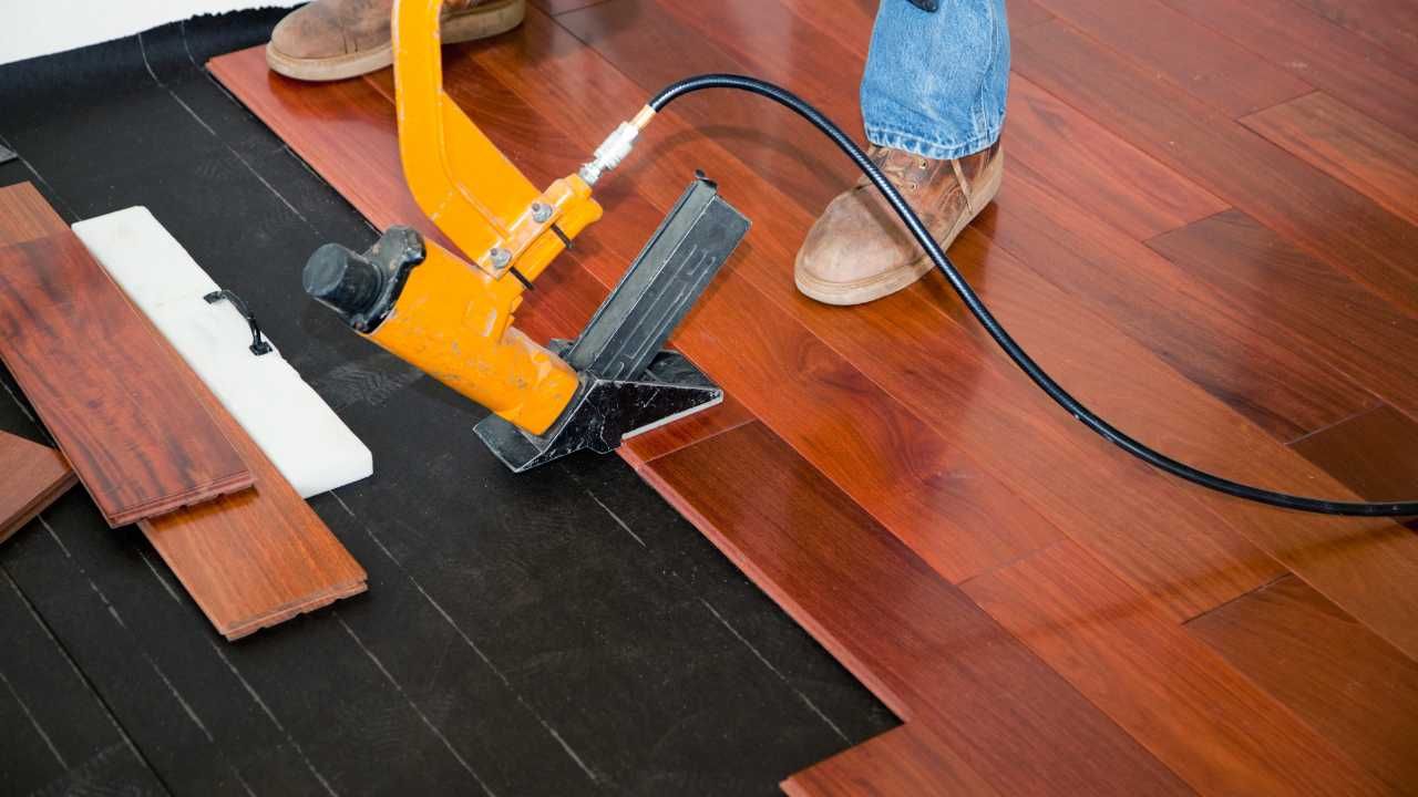 A man operates a power tool while installing wood flooring.