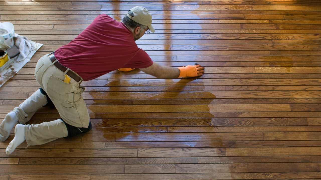 A man carefully applies paint to a wooden floor.