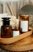 Brown apothecary bottles and a candle on a cork tray, with folded towels and dried flowers in a warm, cozy setting.