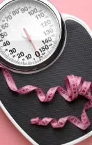A pink measuring tape draped over a black analog bathroom scale set against a solid pink background.