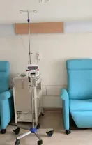 Two light blue medical recliners and mobile IV stands positioned against a white wall in a hospital infusion room.