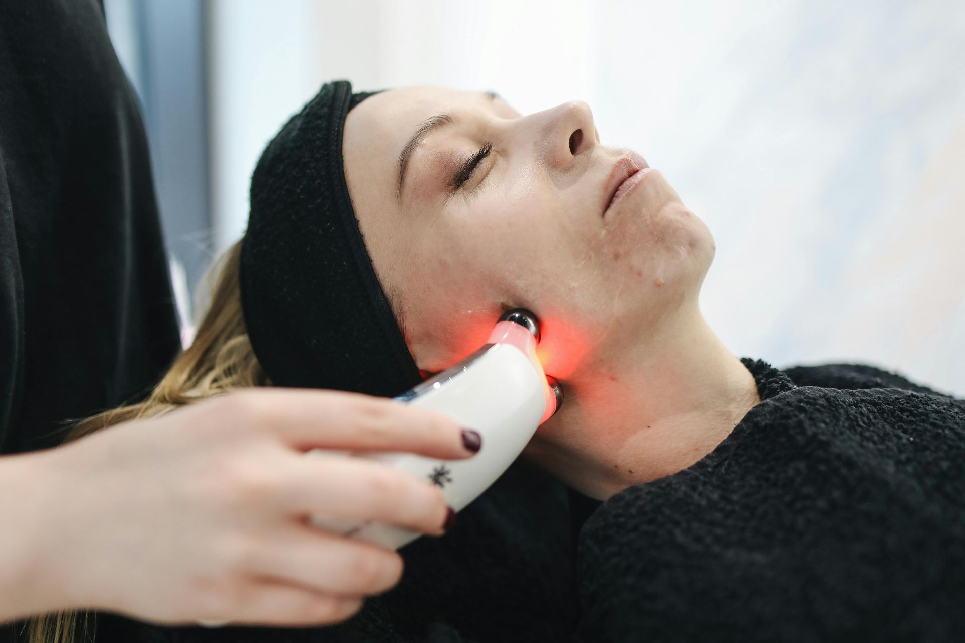 A person receiving a red light facial therapy treatment on their cheek with a handheld device in a spa setting.