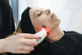 A person receiving a red light facial therapy treatment on their cheek with a handheld device in a spa setting.