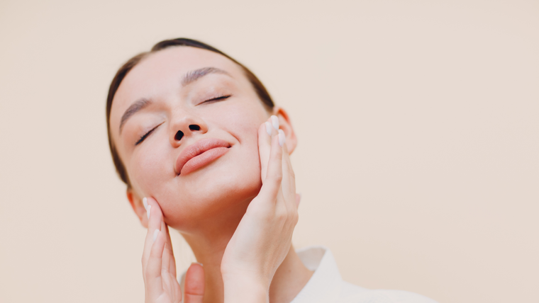 A person with eyes closed gently touches their cheek against a plain beige background.