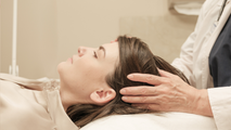 A practitioner gently places their hands on the head of a person lying down in a clinical or therapeutic setting.